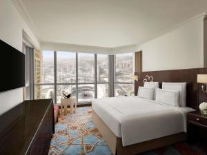 a bedroom with a large white bed and a large window at Swissotel Makkah in Makkah