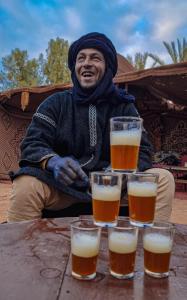 Un hombre sentado en una mesa con cuatro vasos de cerveza. en Auberge la Palmeraie, en Mhamid