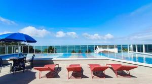 a pool with chairs and tables and an umbrella at Estúdio a 1 min do mar - Mila rooftop in Tamandaré
