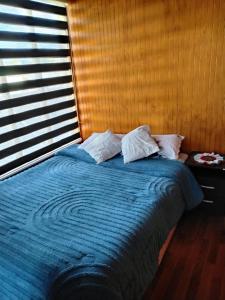 a bed with a blue comforter in a room with a window at Departamento centro Quellon in Quellón