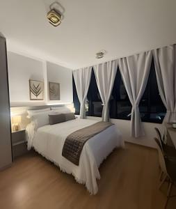 Schlafzimmer mit einem großen weißen Bett und Fenstern in der Unterkunft Essenza Elysia Premium Studio in Curitiba