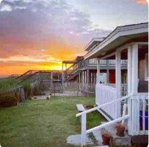 een huis met een veranda met een zonsondergang op de achtergrond bij Egret in Holden Beach