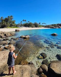 Una niña parada en una playa sosteniendo una caña de pescar en Pet Friendly Sleeps 8 Bowen Holiday House, en Bowen