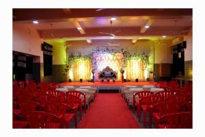 Un salón de banquetes con sillas rojas y un escenario con una mesa. en Kamala Shanti Palace, en Solapur