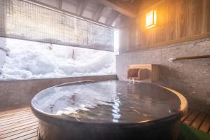 Jozankei Onsen Yurakusoan في Jozankei: حوض استحمام ساخن في غرفة مغطاة بالثلج على النافذة
