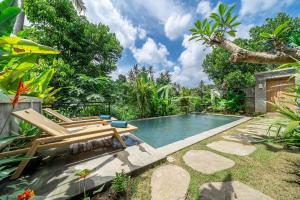 a swimming pool in a garden with two lounge chairs and a pool at Saughina Ubud in Ubud