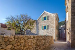 a stone building with green windows and a stone wall at Studio Suites Mila in Komiža