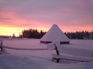 uma casa coberta de neve com um pôr-do-sol ao fundo em Hotel Glamping Gällivare - Laponia Sky Hut - Norrbotten - Lappland - Northern Lights em Koskullskulle