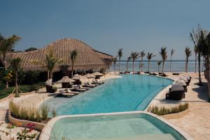 a swimming pool with chairs and umbrellas and the ocean at ARYA Sumba - Kodi Resort in Tambolaka