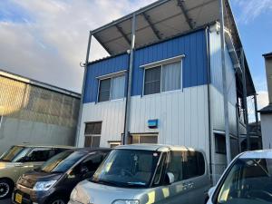 松山一棟貸し宿Tsuji في ماتسوياما: مبنى ازرق وابيض فيه سيارات تقف امامه