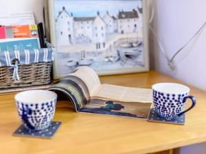 een open boek op een tafel naast twee kopjes bij Pebble Cottage - Uk32243 in Aberdyfi