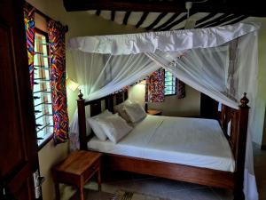 een slaapkamer met een hemelbed met witte lakens en kussens bij Petasha Bustani Villas Diani with pool and parking in Galu