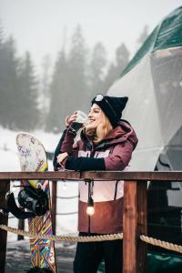 a woman drinking a drink while standing next to a snowboard at Góralski Harem Osada Glamp & Glass z Jacuzzi i Balią in Zakopane