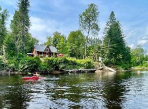 a house on the banks of a river with a red boat at Repère de la Rivière - Bord de l'eau- Activités nautiques in Saint-Alexis-des-Monts