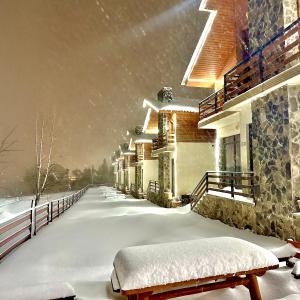 Una acera cubierta de nieve con un banco frente a un edificio. en Villa Mtashi, en Bakuriani