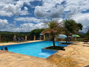 uma piscina com palmeiras, cadeiras e um céu em Pousada São Sebastião em São Sebastião do Rio Verde