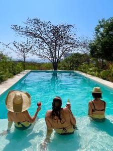Tres mujeres sentadas en una piscina con bebidas en Villa Cuachalalate - Puerto Escondido, en El Puertecito