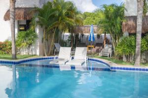 two chairs and an umbrella in a swimming pool at Oasis Tajaja Pousada Boutique na Costa do Conde in Jacumã