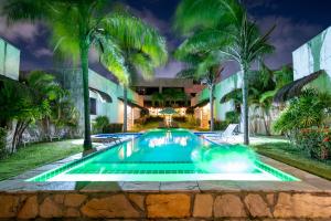 a swimming pool in front of a building with palm trees at Oasis Tajaja Pousada Boutique na Costa do Conde in Jacumã