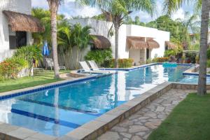 a pool at a resort with two chairs and palm trees at Oasis Tajaja Pousada Boutique na Costa do Conde in Jacumã