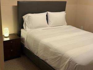 Cama con sábanas blancas y almohadas junto a una mesita de noche en Cozy Private Basement Apartment in Fort Erie, en Fort Erie