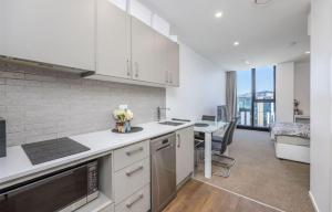 City life Skytower view with Balcony Famliy Retreat في أوكلاند: مطبخ مع دواليب بيضاء وطاولة مع ورد
