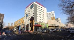 a tall white building with cars parked in a parking lot at Ibis Harbin Normal University in Harbin