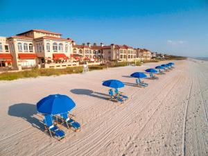 a row of beach chairs with blue umbrellas on the beach at The Lodge & Club at Ponte Vedra Beach in Ponte Vedra Beach