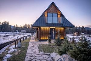 una piccola casa con un tetto nero nella neve di WHITE BROOK Luxury Chalets a Witów