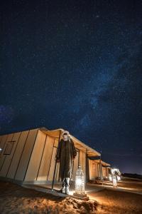a man standing in front of a tent at night at Merzouga dunes erg chabbi Camp in Merzouga