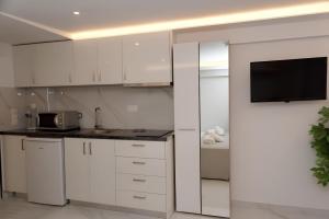 a kitchen with white cabinets and a tv on the wall at IFI Apartments in Paralia Katerinis