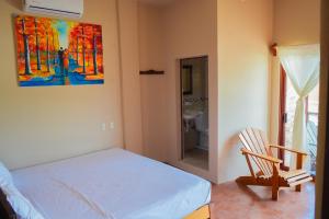 een slaapkamer met een bed en een stoel en een schilderij bij Posada El Mágico in Mazunte