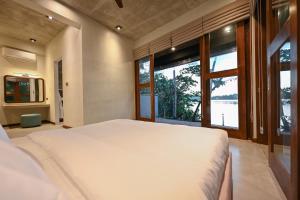 Un dormitorio con una gran cama blanca y grandes ventanales. en Roo Water Villas, en Balapitiya