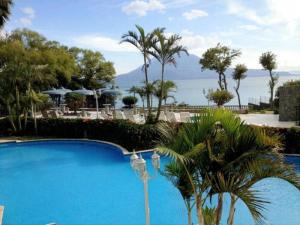a blue swimming pool with palm trees and the ocean at Penthouse con vistas espectaculares del Lago de Atitlán in Panajachel