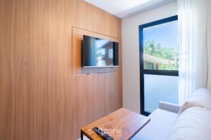 een woonkamer met een tv aan een houten muur bij Studios Modernos a 2km da Praia do Rosa - RSOs in Praia do Rosa +277 foto's