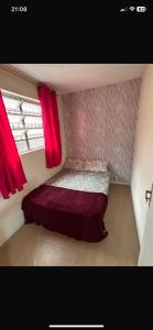 Un dormitorio pequeño con una cama con cortinas rojas. en Hostel San Pietro, en Santos