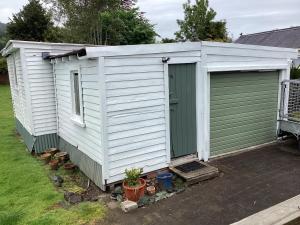 Un cobertizo blanco con una puerta verde y algunas plantas. en Funski Lodge sleeps 10 Where Adventure Begins, en Taumarunui