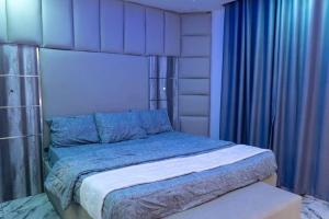 a bedroom with a large bed with blue curtains at Hapton apartment in Abuja