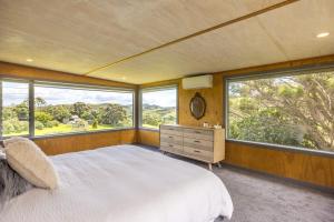 Un dormitorio con una cama grande y grandes ventanales. en Lookout Landing by Waiheke Pure, en Waiheke Island