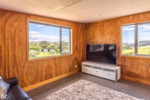 sala de estar con TV de pantalla plana y 2 ventanas en Lookout Landing by Waiheke Pure, en Waiheke Island