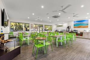 Broome Time Resort في بروم: مطعم فيه كراسي خضراء وطاولات في كفتريا