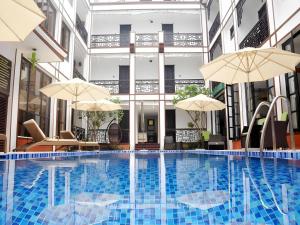 una piscina con sombrillas y sillas y un edificio en Vinh Hung 2 City Hotel, en Hoi An