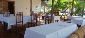 a dining room with white tables and chairs and trees at TheChef NungwiBungalow in Kidoti