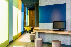 a lobby with a tv and stools in a room at ibis budget Saint Quentin Yvelines - Vélodrome in Montigny-le-Bretonneux