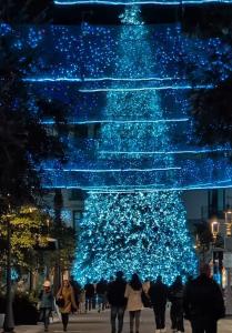 Un árbol de Navidad azul con gente caminando a su alrededor. en Giacarda Suite, en Salerno
