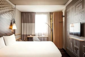 a hotel room with a white bed and a desk at ibis Saint Quentin en Yvelines - Vélodrome in Montigny-le-Bretonneux