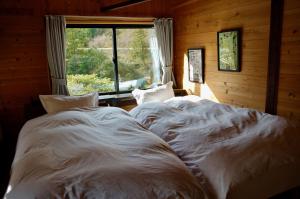 Sakura House サクラハウス 高知駅から車で20分-豊かな自然を味わう山の隠れ家 في كوتشي: سريرين بيض في غرفة مع نافذة