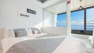 Habitación blanca con 2 camas y ventana grande. en Gangneung The ciel Spa Pension, en Gangneung