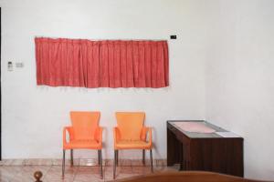 two orange chairs in a room with a red curtain at Nirina Homestay Pringsewu Mitra RedDoorz in Margakaya