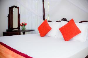 a white bed with red pillows and a mirror at The Cozy Villa in Ambalangoda